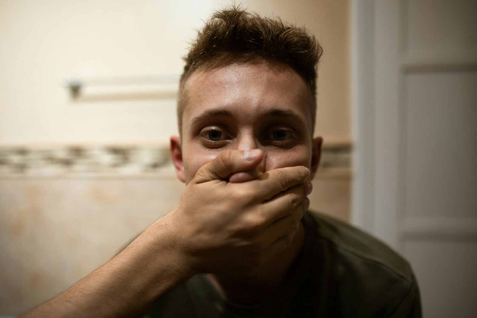 Man being silenced by someone with their hand over his mouth.